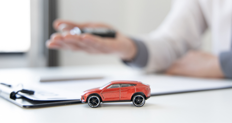 Small model car on a desk with a person holding car keys in the background, representing a car buying decision process